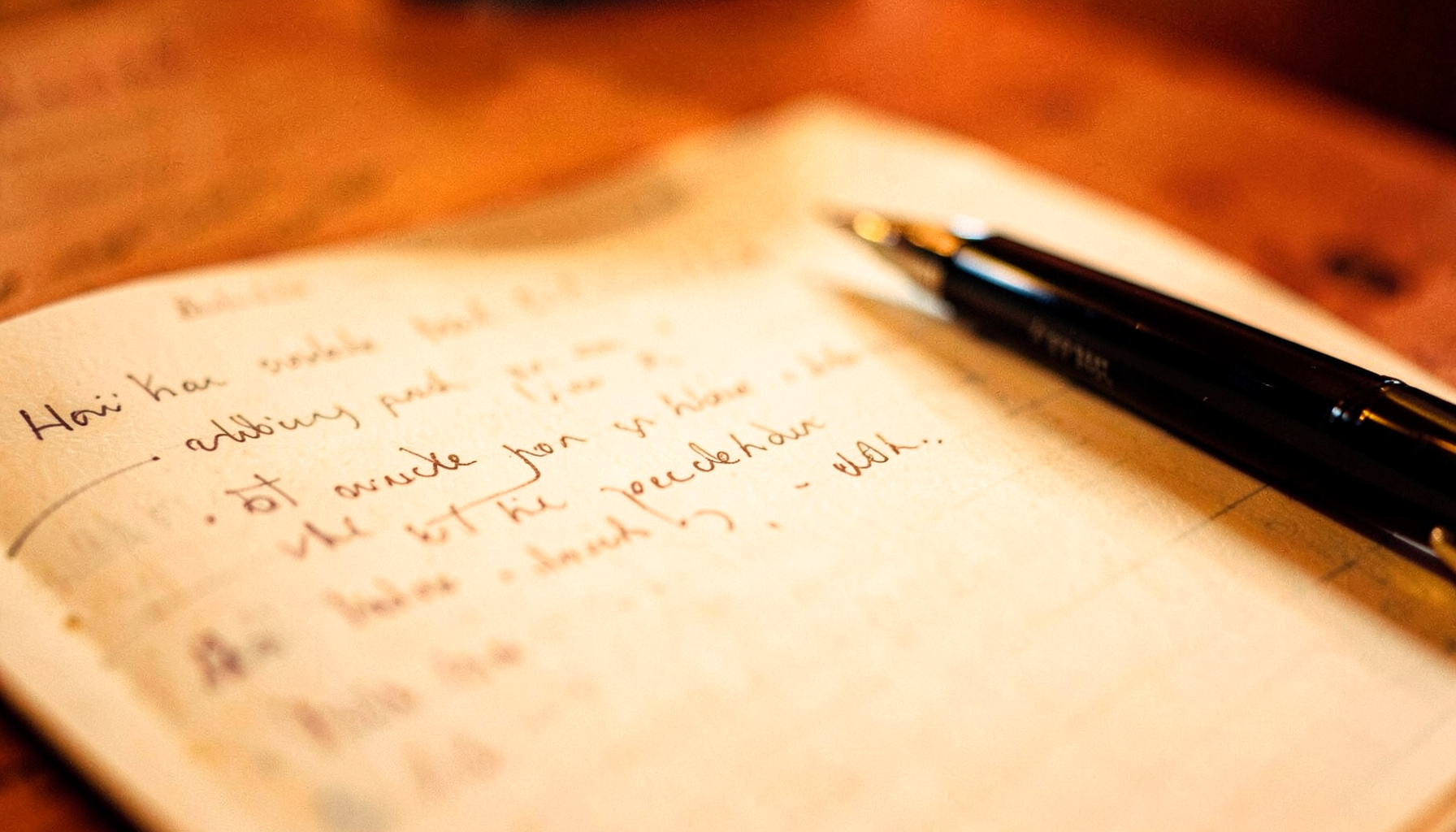 A softly lit close-up of a handwritten notebook page with a pen resting beside it, warm amber and cream tones, contemplative mood.